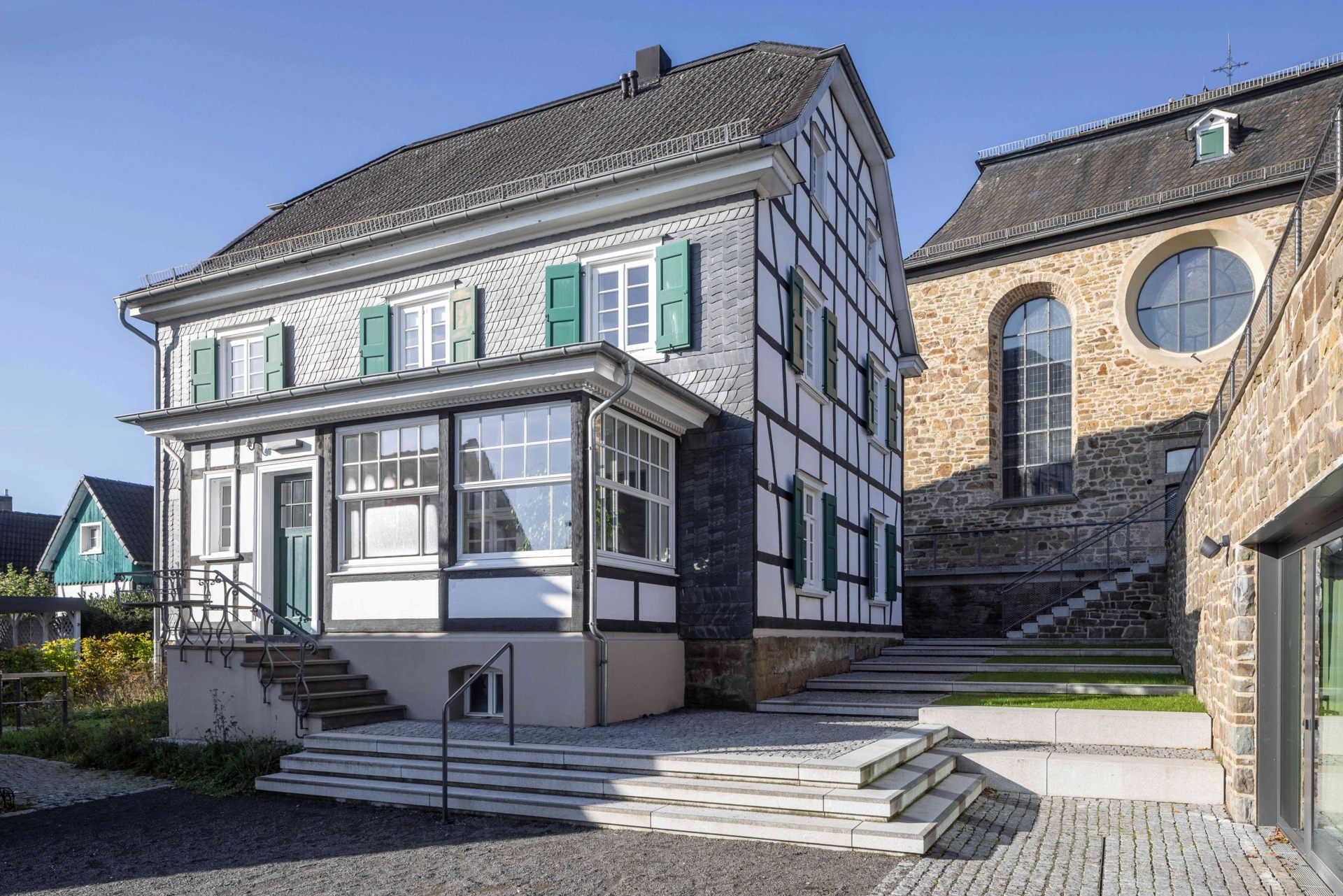 Das Pfarrhaus im Ensemble mit Kirche dahinter und Gemeindezentrum rechts.